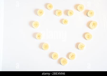 Tranches de morceaux de banane disposées en forme de coeur d'amour sur un fond blanc Uni Banque D'Images
