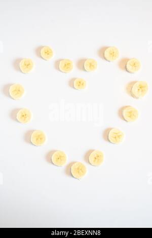 Tranches de morceaux de banane disposées en forme de coeur d'amour sur un fond blanc Uni Banque D'Images