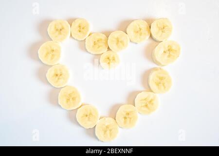 Tranches de morceaux de banane disposées en forme de coeur d'amour sur un fond blanc Uni Banque D'Images