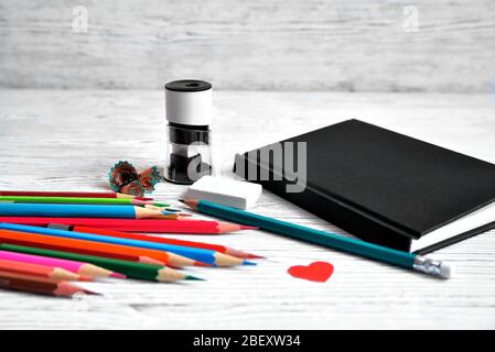 Crayons, bloc-notes, taille-objets, gomme et copeaux de crayons sur un fond gris non uniforme coeur rouge Banque D'Images