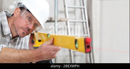 l'homme de la construction mesure avec laser de niveau porter un casque et des lunettes de protection sur le site du bâtiment intérieur Banque D'Images