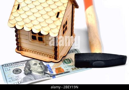 Maison en bois, un billet de 100 dollars et un marteau sur fond blanc, isoler Banque D'Images