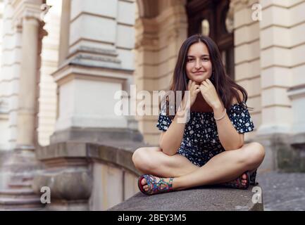 Fille brunette assise dans la vieille ville. Fille en été robe d'une journée ensoleillée Banque D'Images