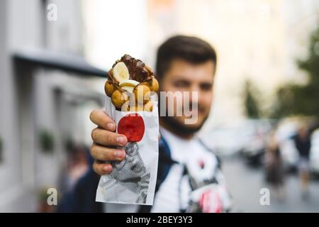 Jeune homme tenant des gaufres avec de la glace, des bananes et du chocolat Banque D'Images