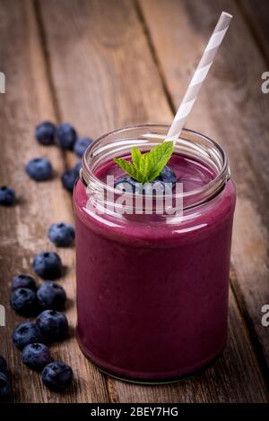 Smoothie aux bleuets dans un bocal en verre avec paille et branche de menthe, sur une table en bois vintage avec baies fraîches. Banque D'Images