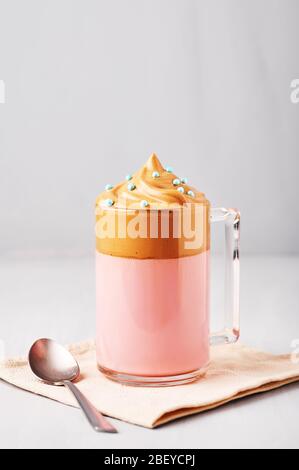 Lait rose Dalgona café décoré de saupoudrer de Pâques bleues dans une tasse en verre à fond gris clair. Le café Dalgona est un verre à la mode coréen Banque D'Images