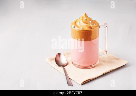 Lait rose Dalgona café décoré de saupoudrer de Pâques bleues dans une tasse en verre à fond gris clair. Le café Dalgona est un verre à la mode coréen Banque D'Images