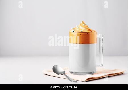 Le café Dalgona est décoré de saupoudrer de Pâques bleues dans une tasse en verre à fond gris clair. Le café à la mode Dalgona est un verre à la mode coréen avec fouet Banque D'Images