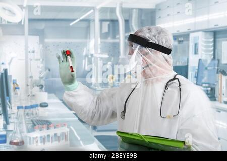Médecin portant un masque respiratoire et tenant l'échantillon sanguin de Covid-19 de Coronavirus. Médecin travaillant avec des échantillons de sang dans un laboratoire hospitalier Banque D'Images