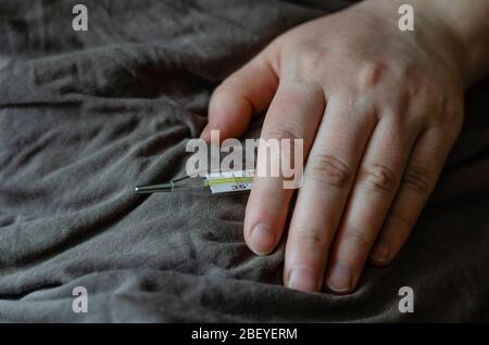 La main féminine repose sur une couverture. Dans sa main est un thermomètre au mercure. Le concept est le repos du lit, le traitement, la mesure de la température. Prise de vue au niveau des yeux. Banque D'Images