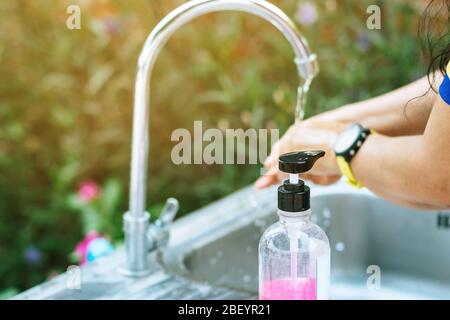 Une femme se lavant les mains du robinet avec du savon rose dans une baignoire en aluminium. Concepts du virus de la grippe, Covid-19 (maladie du coronavirus). Focalisation sélective sur le savon b Banque D'Images