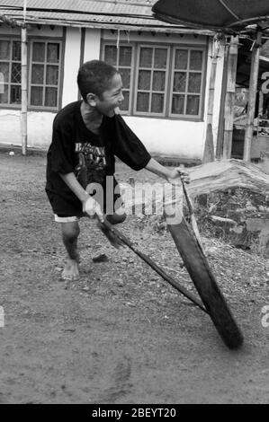 Kelimutu, East Nusa Tenggara / Indonésie - 13 janvier 2015 : portrait d'un garçon dans un village traditionnel jouant avec une roue comme jouet. Noir et blanc Banque D'Images