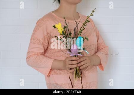 Une jeune fille dans un t-shirt rose contient un bouquet de branches de Pâques avec des œufs de poulet et un lapin sur le fond de mur blanc. Vue horizontale Banque D'Images