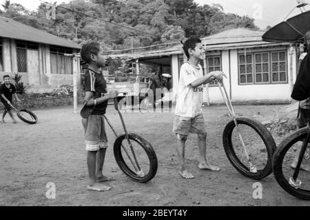 Kelimutu, East Nusa Tenggara / Indonésie - 13 janvier 2015 : portrait d'un garçon dans un village traditionnel jouant avec une roue comme jouet. Noir et blanc Banque D'Images