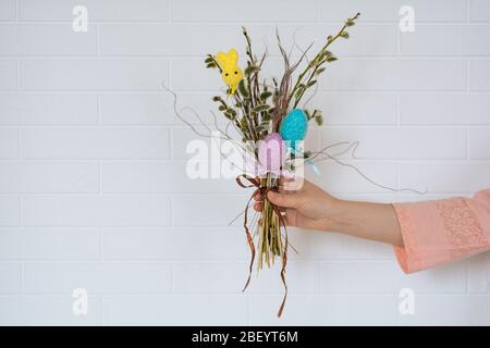 Une jeune fille dans un t-shirt rose contient un bouquet de branches de Pâques avec des œufs de poulet et un lapin sur le fond de mur blanc. Vue horizontale. Fermer Banque D'Images