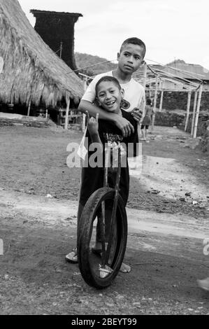 Kelimutu, East Nusa Tenggara / Indonésie - 13 janvier 2015 : portrait d'un garçon dans un village traditionnel jouant avec une roue comme jouet. Noir et blanc Banque D'Images