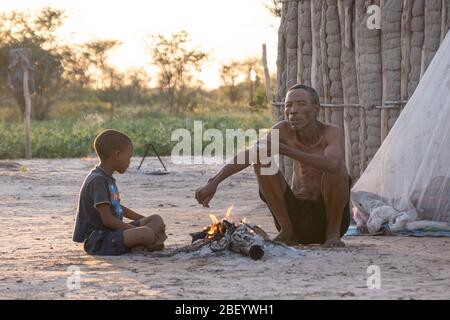 Le chef Gǂkao et son fils partagent un moment de feu à l'aube dans le village de Deng//e à Nyae Nyae, en Namibie. Banque D'Images