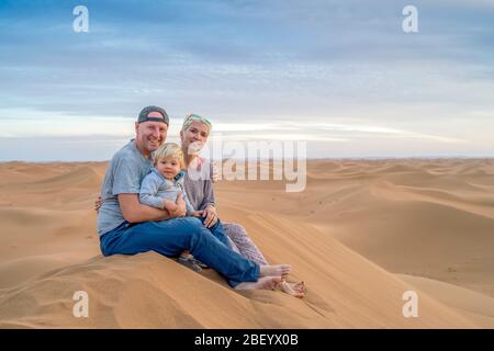 Mère, père et garçon de 2 ans assis sur la dune de sable, désert du Sahara, Maroc Banque D'Images
