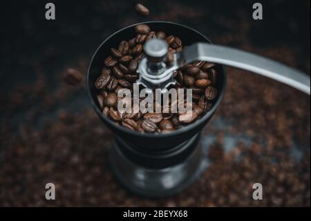 Les grains de café frits tombent dans une mouture manuelle. Couleurs sombres cinématographiques. Préparation de boissons fraîches café du matin pour le petit déjeuner. Meule Banque D'Images