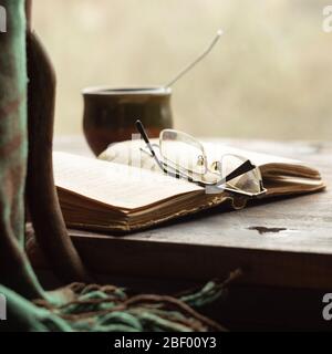 Tasse de café, vieux livre et verres sur le seuil de la fenêtre, près d'une chaise avec un plat. Style rétro Banque D'Images