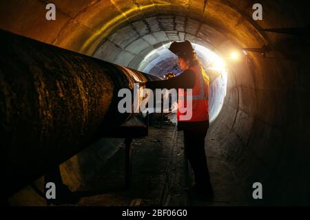 Le travailleur du tunnel examine le pipeline dans le tunnel souterrain Banque D'Images