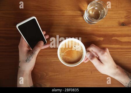 Vue de dessus des mains mâles à l'aide d'un smartphone avec écran vide, copyspace. Surf, shopping en ligne, défilement, Paris, travail. Éducation, freelance, art et concept d'affaires. Café en buvant. Banque D'Images