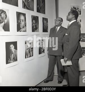 1950, historique, deux invités africains adaptés à une exposition de photographie debout regardant une sélection de photos de la Gold Coast prises à cette époque, Londres, Angleterre, Royaume-Uni. La Gold Coast en Afrique de l'Ouest était une colonie britannique de 1821 jusqu'à son indépendance en 1957. Banque D'Images