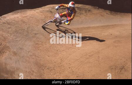 1970, un pilote BMX sur un virage sur une piste de terre ou de gravier prenant part à la course à vélo. BMX est un sport de course de vélo tout-terrain et le nom « BMX » vient du raccourcissement de « motocross de vélo » et a commencé dans les années 70 lorsque les enfants ont commencé à courir des vélos sur des pistes de terre en Californie du Sud. Banque D'Images