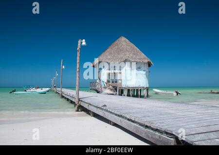 Jetée en bois avec petit palapa en chaume, bateaux de pêche en arrière-plan, mer des Caraïbes et le ciel turquoise Banque D'Images