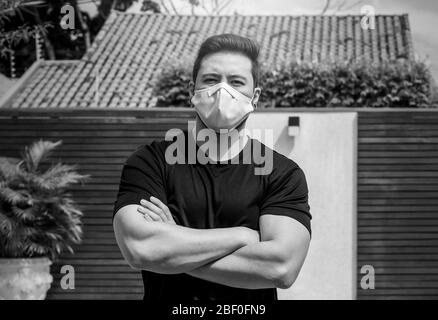 Portrait d'un homme adulte avec des bras croisés portant un masque de visage blanc pendant la quarantaine à la maison. Photo en noir et blanc. Banque D'Images