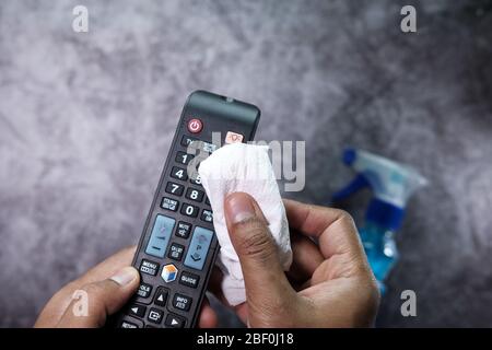 f mains de l'homme utilisant un chiffon humide pour désinfecter la télécommande du téléviseur. Banque D'Images