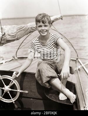 1930 SOURIRE TOWHEDEED ENTHOUSIASTE BAREPOWED GARÇON ASSIS AU SPOKED CAST BATEAUX ROUE VOLANT PILOTAGE PETIT VOILIER - B4213 HAR001 HARS INSPIRATION PLEINE LONGUEUR HOMMES RISQUE BATEAUX CONFIANCE VOILIER TRANSPORT EXPRESSIONS B&W OEIL CONTACT RÊVES BONHEUR AVENTURE GAIE LOISIRS SAVOIR DIRECTION GUIDE FIERTÉ ENTHOUSIASTE À L'OCCASION LES SOURIRES PIEDS NUS CONNEXION CONCEPTUEL JOYEUSE SOLITAIRE ÉLÉGANT PILOTING BASE CROISSANCE JEUNES PRÉ-ADOLESCENCE PRÉ-ADOLESCENCE GARÇON RELAXATION NOIR ET BLANC FONTE CAUCASIENNE ETHNICITÉ HAR001 ANCIEN FAÇONNÉ Banque D'Images