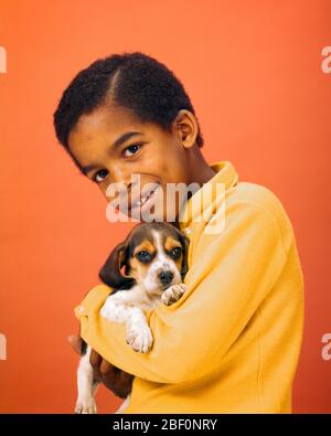 ANNÉES 1970 UN GARÇON AFRO-AMÉRICAIN HEUREUX PORTANT UN MAILLOT JAUNE TENANT UN CHIOT DE CHIEN DE BEAGLE SOURIANT REGARDANT LA CAMÉRA - KD3549 PHT001 HARS LES HOMMES BIENVEILLANTS ANIMAUX CONTACT YEUX BONHEUR MAMMIFÈRES JOYEUX BEAGLE AFRO-AMÉRICAINS LES CHIENS AFRO-AMÉRICAINS EXCITATION NOIRE ETHNICITÉ NOIRE SOURIRE FIERTÉ POOCH CONNEXION RESPONSABILITÉ SYMPATHIQUE JOYEUX CANINE JEUNES MAMMIFÈRES VIEUX AMÉRICAINS À L'ANCIENNE GÉNÉRATION Banque D'Images