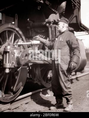 HOMME DES ANNÉES 1930 TECHNICIEN DE TRAVAIL FERROVIAIRE PORTANT DES GANTS DE TRAVAIL AVEC DES ENGRENAGES À HUILE SUR LA ROUE MOTRICE DU MOTEUR À VAPEUR DU TRAIN - R6180 HAR001 EMPLOIS HARS ESPACE DE COPIE PERSONNES DE LONGUEUR COMPLÈTE HOMMES PROFESSION TRANSPORT MILIEU-ÂGE B&W HOMME D'ÂGE MOYEN COMPÉTENCES FERROVIAIRE PROFESSIONNELLES COMPÉTENCES ENGINS DE PROTECTION CARRIÈRES TRAVAIL SUR LES PROFESSIONS DE L'EMPLOI ENTRETIEN DES CONNEXIONS FERROVIAIRE EMPLOYÉ ADULTE MOYEN ADULTE HOMME ADULTE MILIEU DE L'ÂGE ADULTE LUBRIFICATION NOIR ET BLANC CAUCASIEN ETHNICITÉ HAR001 LABOURANT À L'ANCIENNE Banque D'Images