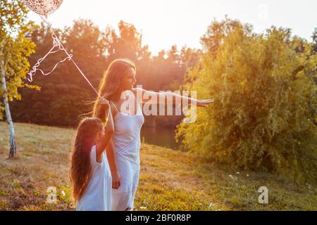 Fête des mères. Mère et fille tenant des balons marchant dehors. Famille s'amuser dans le parc de printemps Banque D'Images