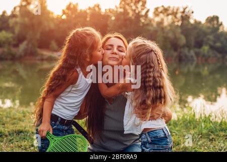 Fête des mères. Les enfants embrassent la mère sur la joue. Famille marchant dans le parc de printemps près du lac après avoir joué au badminton.