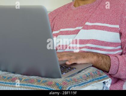 Espace de travail de fortune où un homme adulte travaille de sa chambre avec un oreiller pour soutenir son ordinateur portable pendant la pandémie de covid-19, Suède Banque D'Images