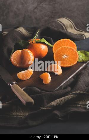 Oranges ou tangerines mandarines fraîches avec feuilles sur fond sombre texturé Banque D'Images