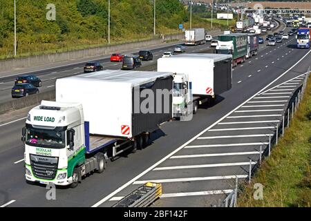En regardant vers le bas sur la circulation en marche arrière sur l'autoroute M25 très fréquentée derrière deux camions chargés d'un bâtiment modulaire à grande capacité de charge Angleterre Royaume-Uni Banque D'Images
