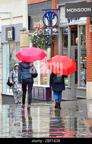 Pluie deux femmes marchent par temps humide dans le centre-ville piétons seulement les acheteurs zone de rue dans la pluie sous le parapluie rouge et réflexions Durham Angleterre Royaume-Uni Banque D'Images