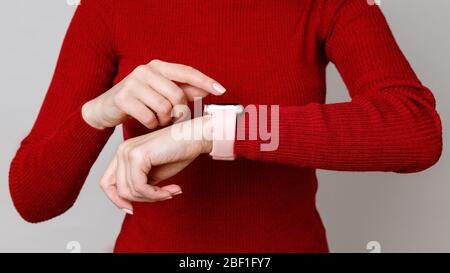 Photo courte de la femme touchant, en plaçant ou en utilisant sa montre intelligente sur son poignet, en vérifiant le temps, sur fond de col de cygne rouge Banque D'Images