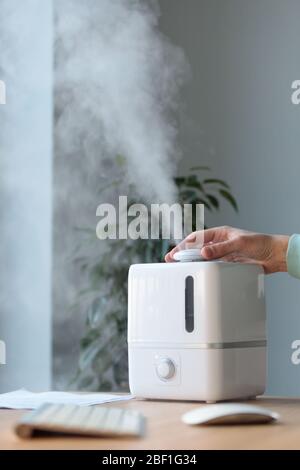 Homme utilisant un diffuseur d'huile aromatique sur la table, vapeur de l'humidificateur d'air, mise au point sélective. Augmentation de l'humidité de l'air à l'intérieur, lieu de travail confortable, Mo Banque D'Images