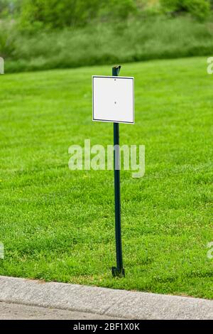 Photo verticale d'un panneau vierge devant une cour avec de l'herbe verte. Banque D'Images