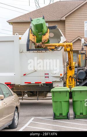 Tir vertical d'un camion à ordures avec un bras de robot qui dévidage les déchets d'un conteneur de déchets résidentiel. Banque D'Images