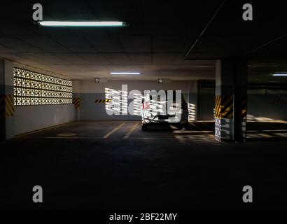 Scène panoramique d'une voiture blanche garée seul sur le parking souterrain, soleil du coucher du soleil, ombre de soleil.voiture garée dans un garage privé ou un parking commercial. Banque D'Images