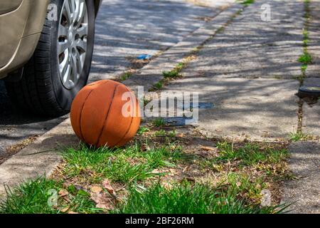 Un basket-ball abandonné légèrement dégonflé sur une rue de banlieue Banque D'Images