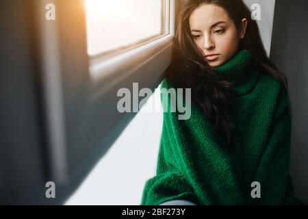 la jeune femme mécontente est triste près de la fenêtre. La brunette pleure. Tristesse, apathie, dépression et mélocilie. Banque D'Images