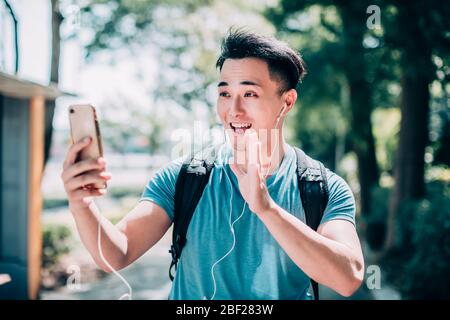 un jeune homme heureux qui marche dans la rue et utilise un téléphone portable Banque D'Images
