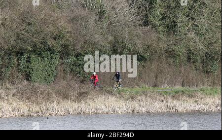 Cycliste femelle vêque de couleur rouge et cycliste mâle longeant l'ancien chemin de remorquage du canal au début du printemps, à côté du tronçon Broadwater de l'ancien canal Lagan. Banque D'Images