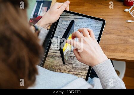 Paris, France - 16 avril 2020: Femme curieuse regarder sur le site Internet d'Apple Computers sur iPad Pro tablette nouvelle inspection iPhone se sur l'écran réalité augmentée Banque D'Images